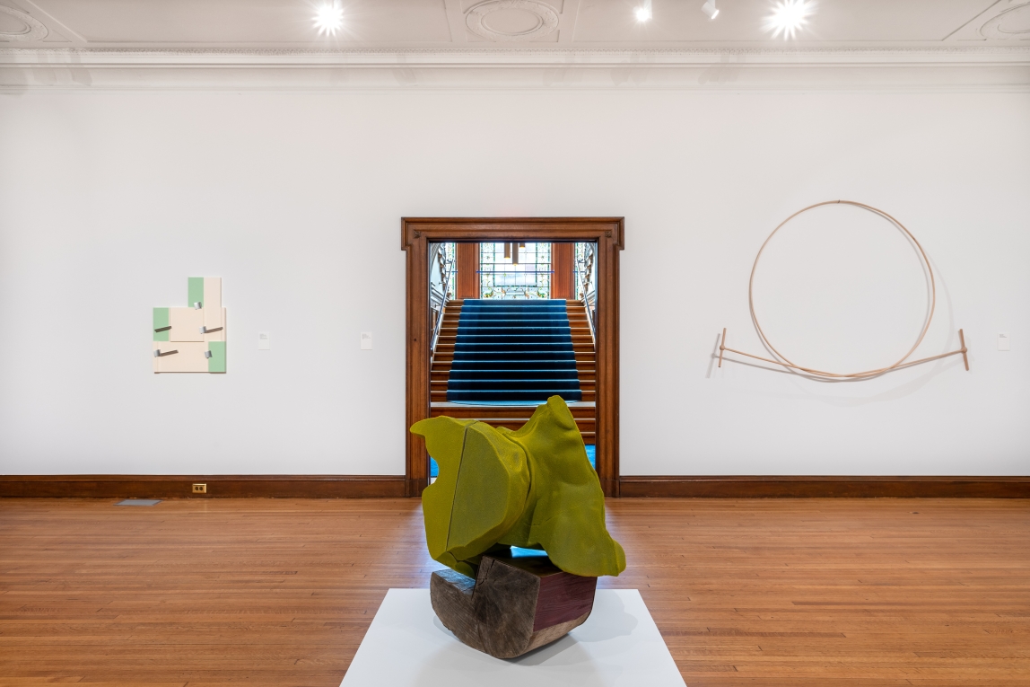 Installation view of gallery with sculpture in middle and two works hanging on wall