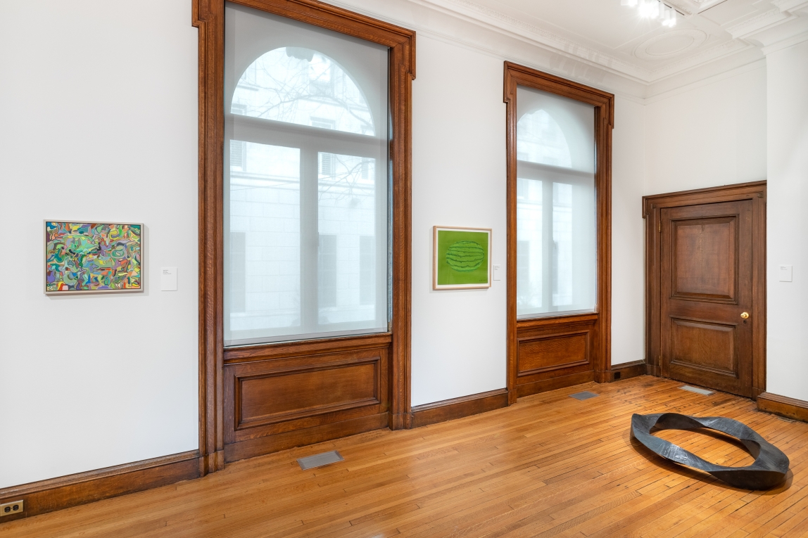 Installation view of two paintings and two windows with a metal ring sculpture on the floor