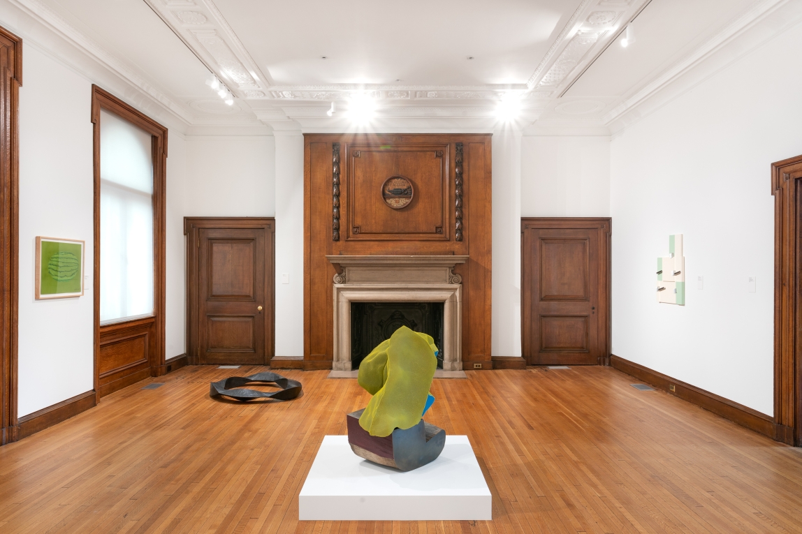 Installation view with two sculptures on ground and two works hanging on opposing walls