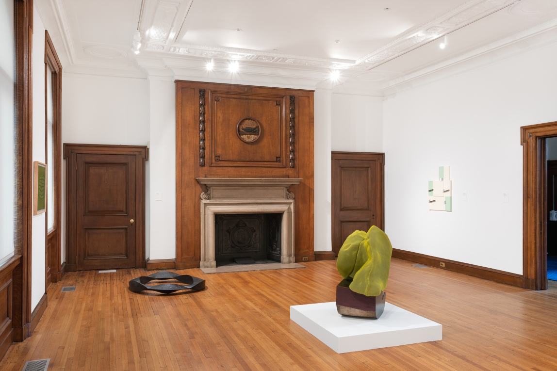 Installation view of two sculptures on ground and two works visible on walls