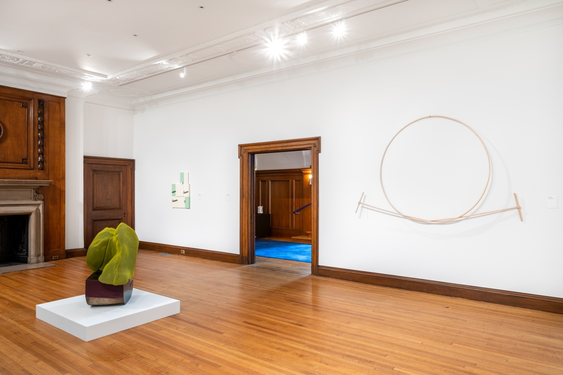 Installation view with green sculpture in foreground and two works hanging on back wall