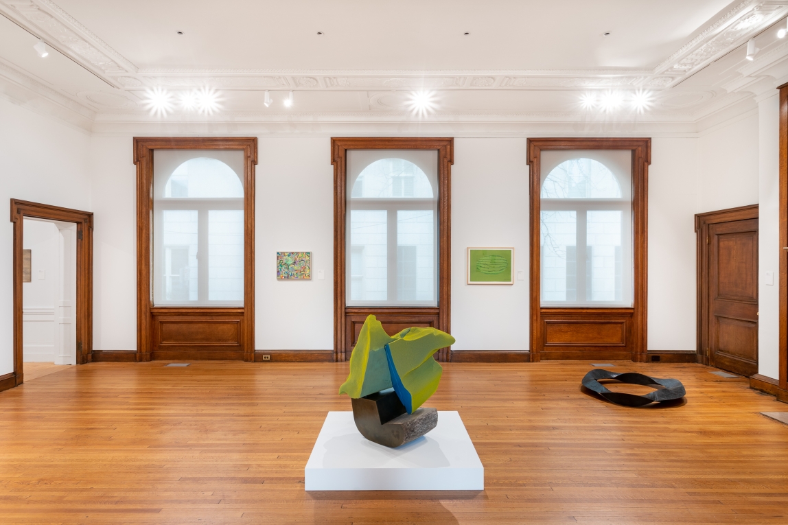 Installation view showing two sculptures on ground and three windows with paintings hung in-between