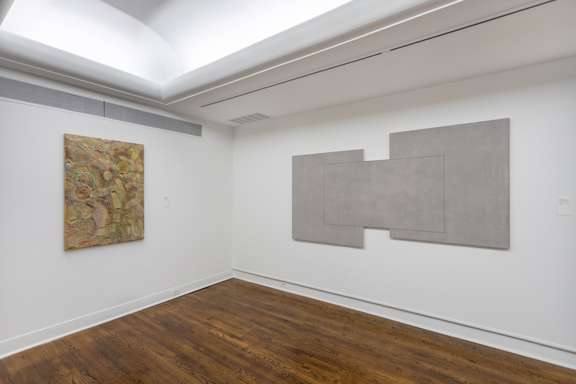 Installation view of large grey painting hanging across from a mixed media work