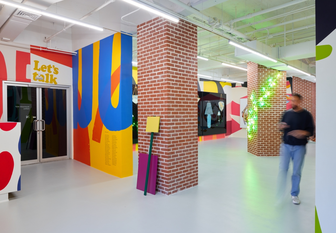 Installation view of brightly colored gallery and blurry figure to the side