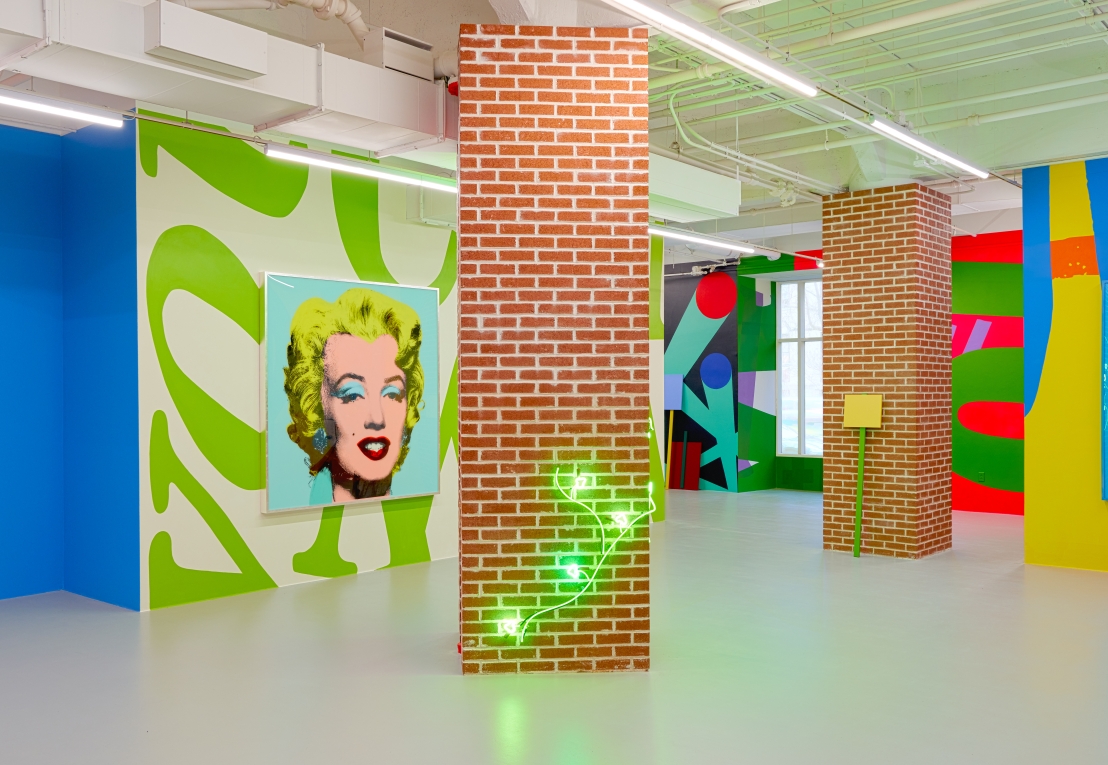 Installation view of The Street with large painting of Marilyn Monroe in background, brick column with neon in foreground