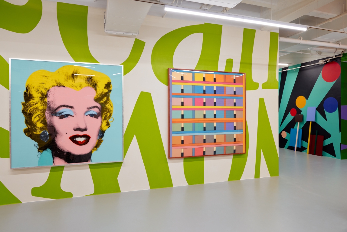 Installation view of large Marilyn Monroe painting next to a painting with cels and colors