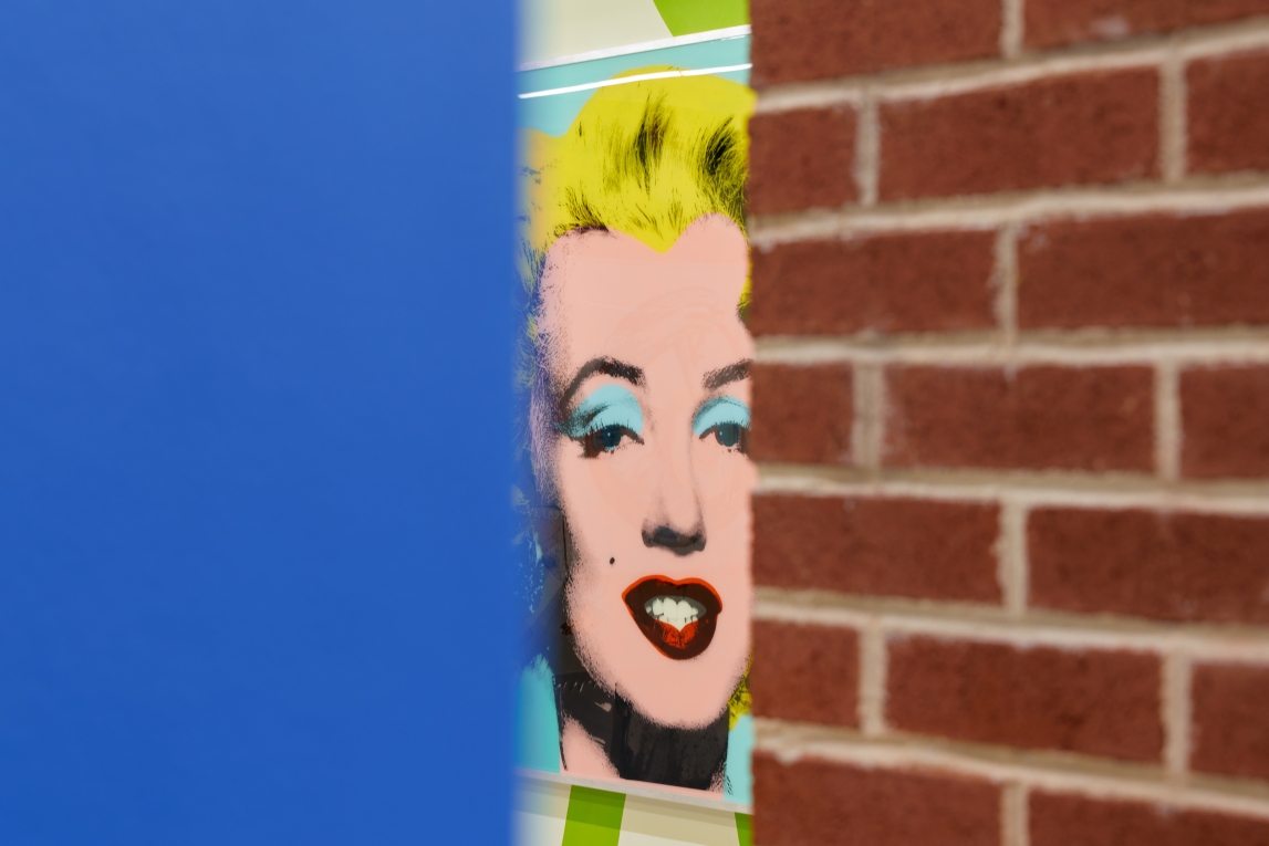 Installation view of The Street with a sliver of Marilyn Monroe painting visible between blue wall and brick column