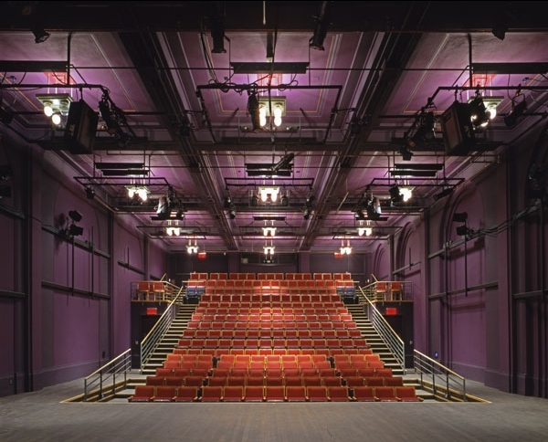 interior of arts bank theater. the ornate walls of the chamber are painted purple and covered in lighting trusses. a large flight of rising red seating is seen dead-on from the stage.