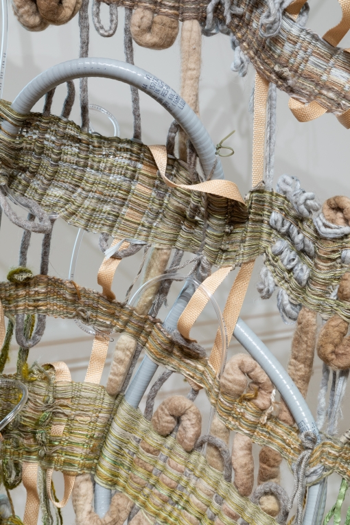Close-up view of woven multi-fiber artwork with yarn, ribbon and tubing