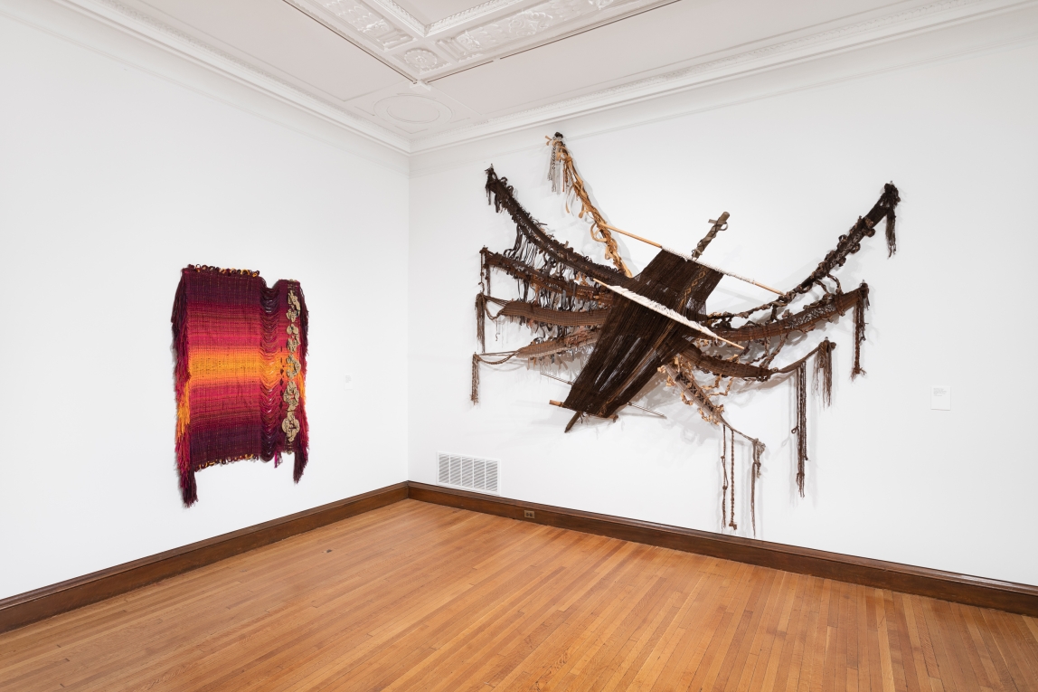 Installation view of two woven fiber artworks hanging on adjoining walls