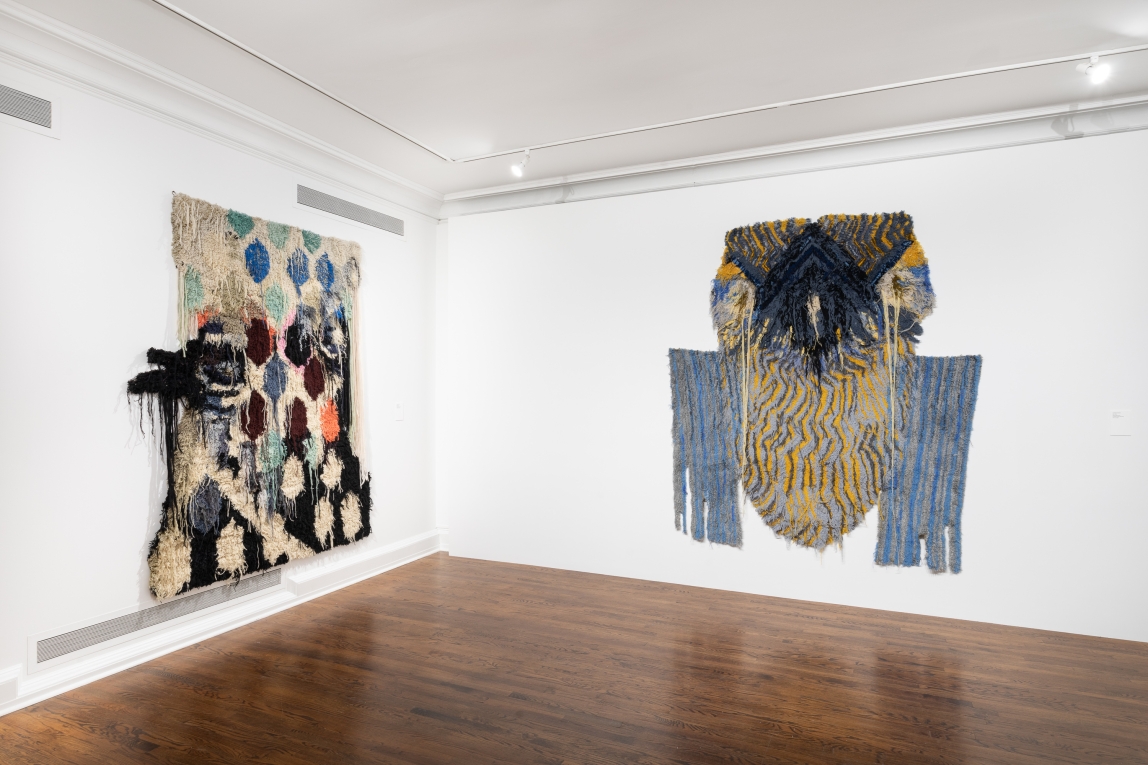 Installation view of two fiber artworks hanging on adding walls