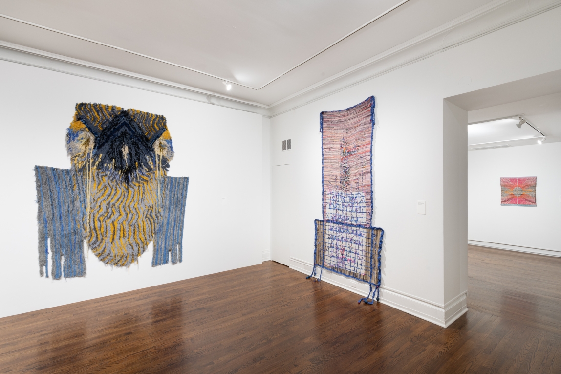 Installation view of large fiber artworks in foreground and smaller one visible through doorway