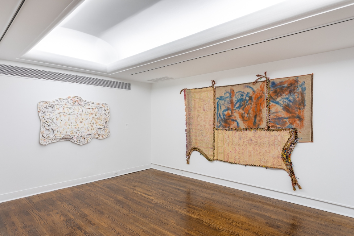 Installation view of two fiber artworks hanging on adjoining walls, one with board and white paint, the other of multiple mats woven together