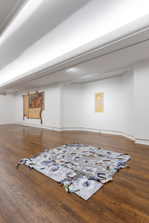 installation view of fiber artwork on floor in foreground and two other works in background