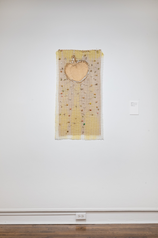 Installation view of woven fiber artwork with beads and a palm fan incorporated into it