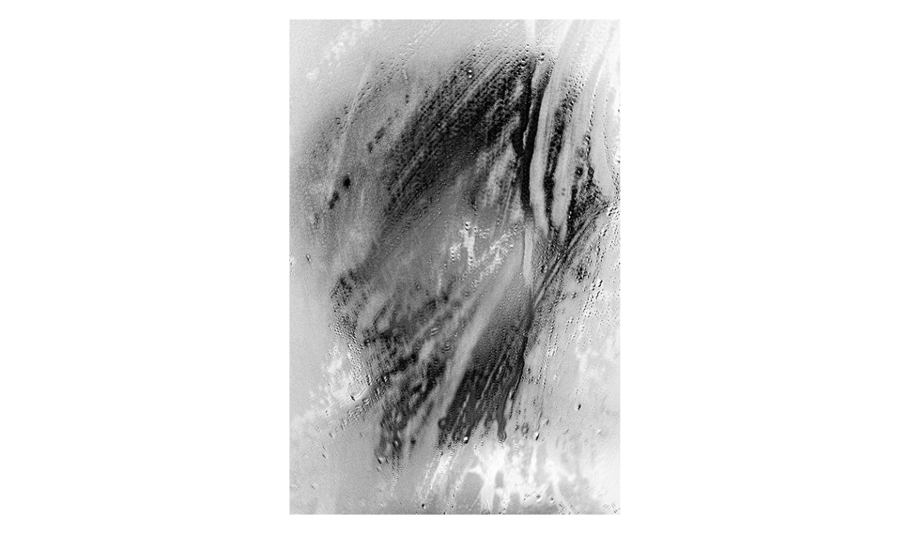 photography a blurry steam and dampness-streaked mirror with a dark vaguely face-like form appearing beneath the steamy wet smudging. 