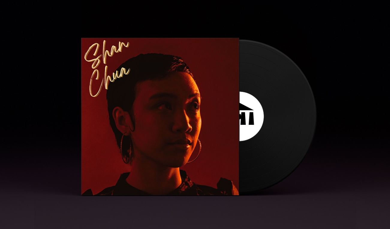 A stylized vinyl record album cover with a black record stamped with the UArts logo poking out. On the sleeve is student Shan Chua in warm ochre tones with a glowing orange light across Chua's face. Chua is looking towards the light. 