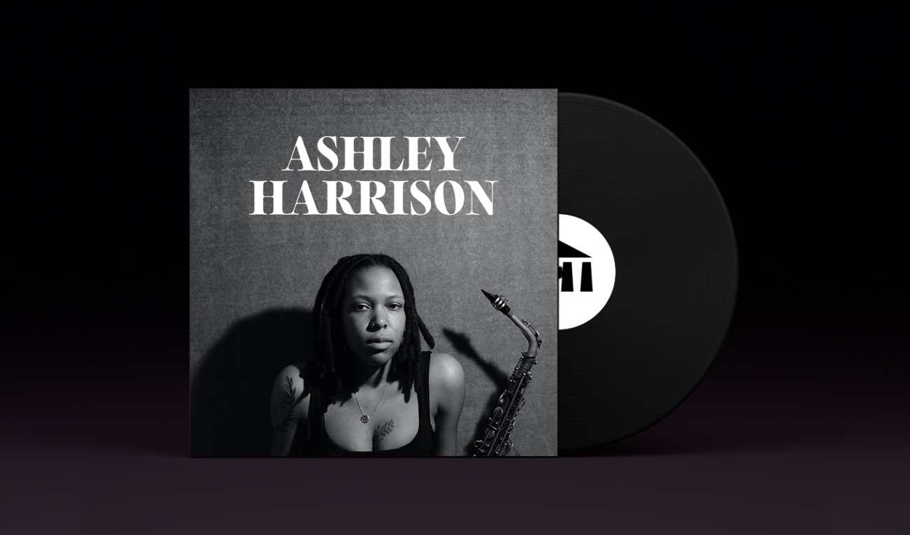 A stylized vinyl record album cover with a black record stamped with the UArts logo poking out. On the sleeve is student Ashley Harrison depicted in black and white holding a saxophone. harrison has long black dreads and a black tank top showing off botanical tattoos. 