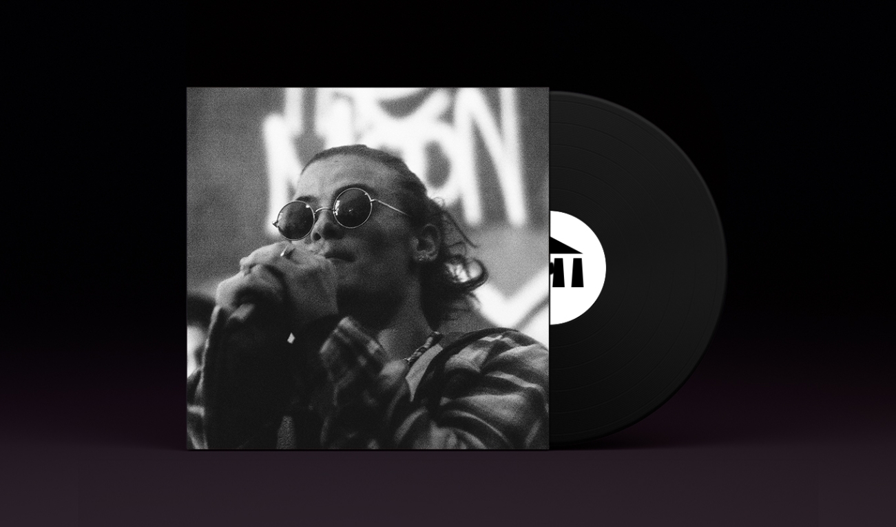A stylized vinyl record album cover with a black record stamped with the UArts logo poking out. On the sleeve is student anthony santosusso in black and white in a flannel shirt and circular sunglasses clutching a mic at mouth level