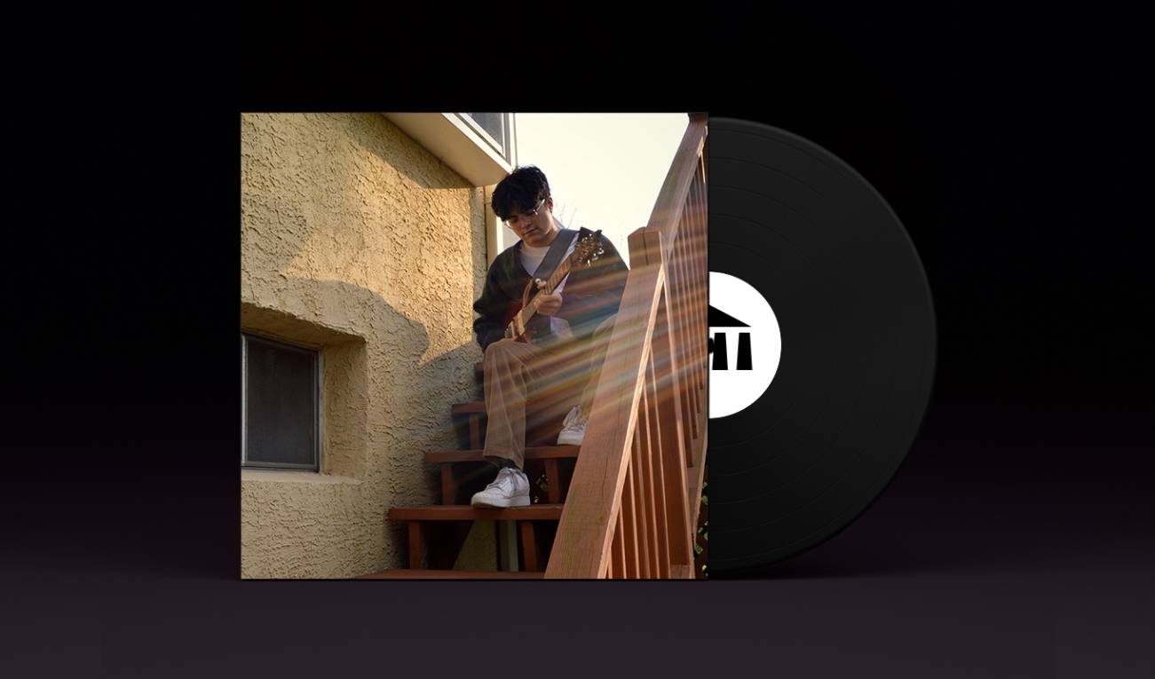 A stylized vinyl record album cover with a black record stamped with the UArts logo poking out. On the sleeve is student noah uy seated in khaki pants and a cardigan on a wooden outdoor staircase playing a guitar. 