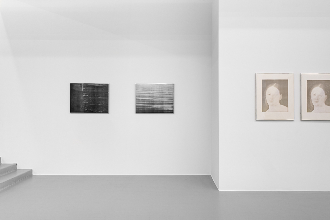Installation view of two black and white images on back wall, and two images of a woman's face in foreground