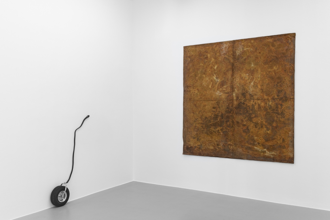 Installation view of two artworks- one latex work hanging on a wall and a small tire with leash on adjacent wall