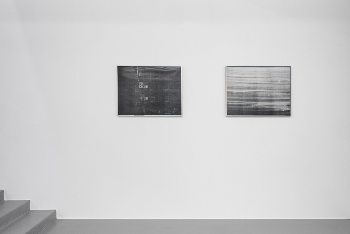 Installation view of two works in black, white and gray hanging on a white wall