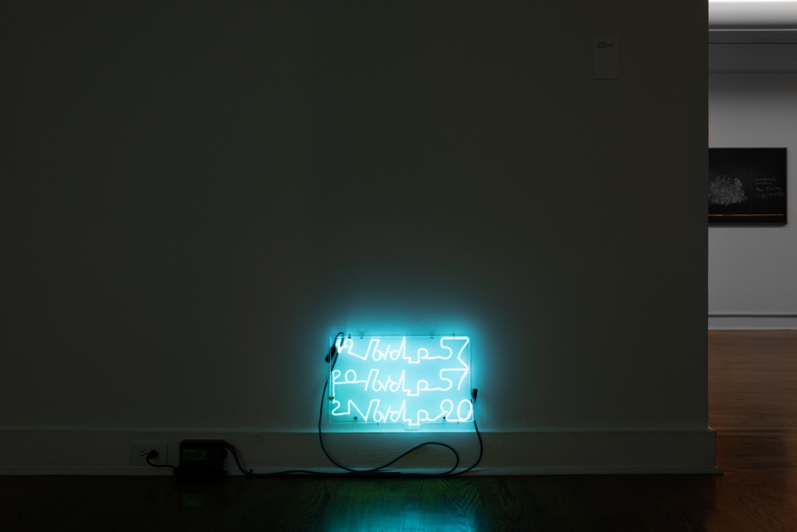 Installation view of neon artwork composed of words installed along gallery floorboard