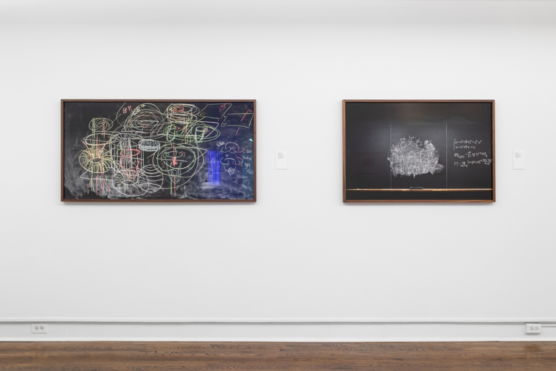 Installation view of two works depicting chalkboards with writing