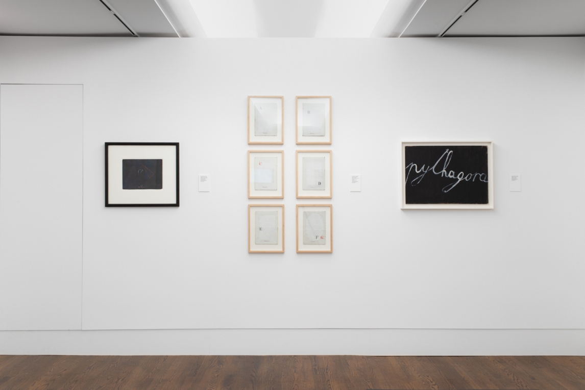 Installation view of a series of six works arranged in two columns, framed by two other works, all consisting of text and letters