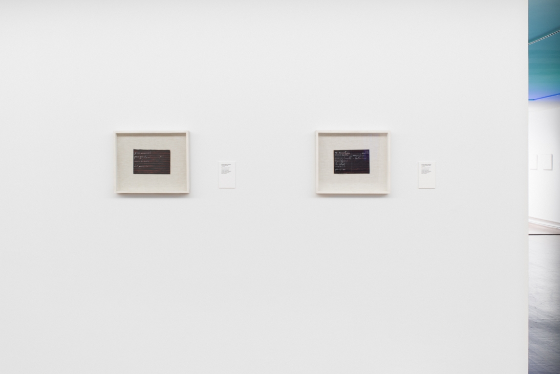 Installation view of two framed artworks depicting text and/or letters on a dark background