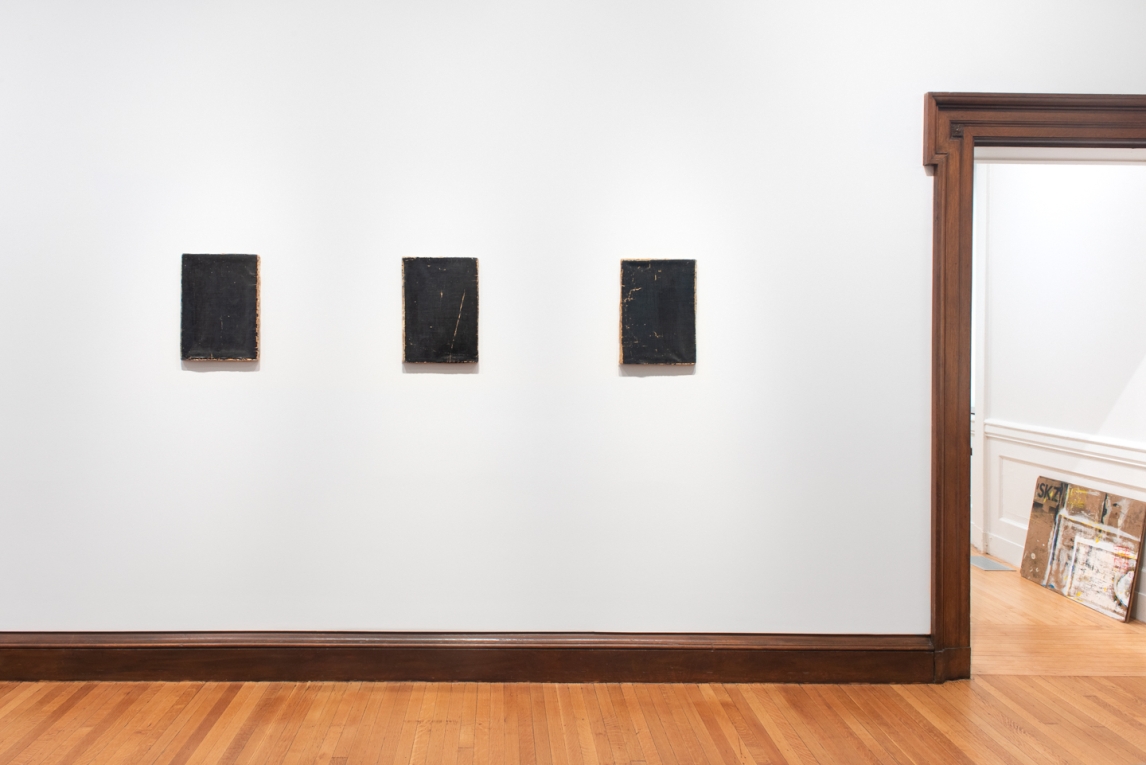 Installation view of three small black paintings hanging in a row on wall