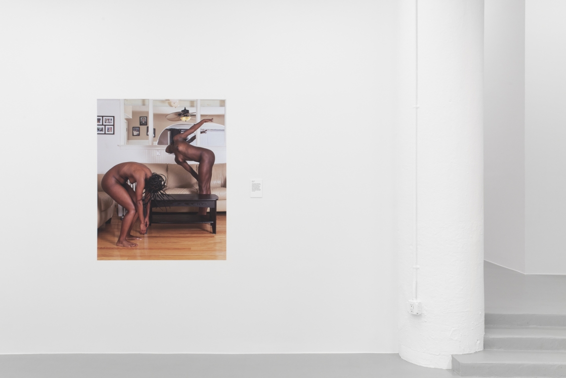 Installation view of vinyl image depicting two Black people in motion, nude in a room in a house