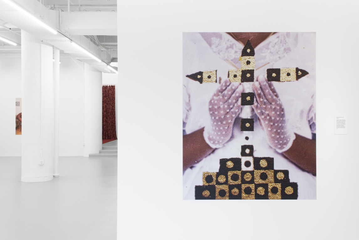Installation view of a vinyl image showing a Black person in white gloves and a white dress holding adorned cross-like object