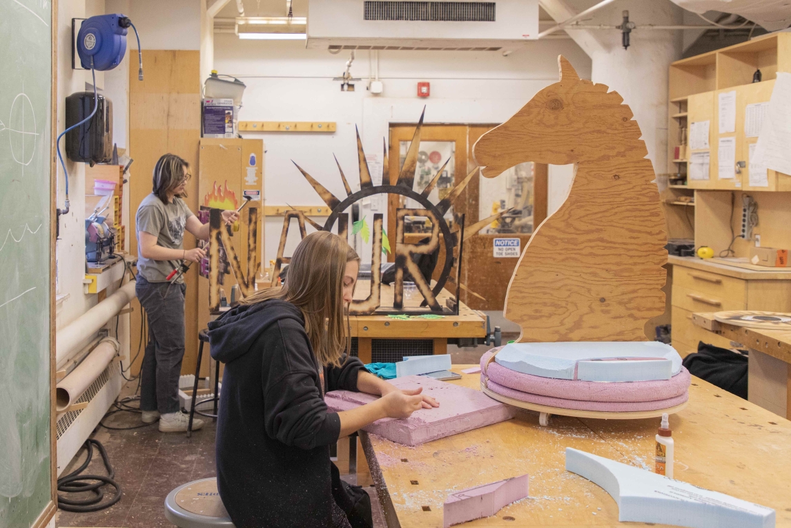 Two students working in sculpture studio one working on a wooden horse 