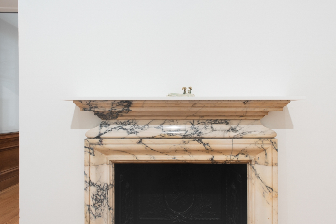 Small sculptural figure sitting on white shelf atop a marble fireplace
