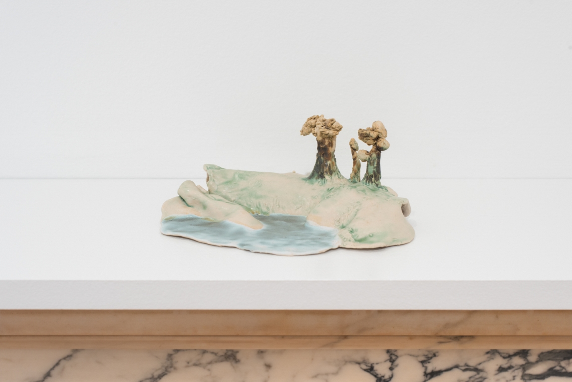 Small sculptural landscape figure sitting on a white shelf 