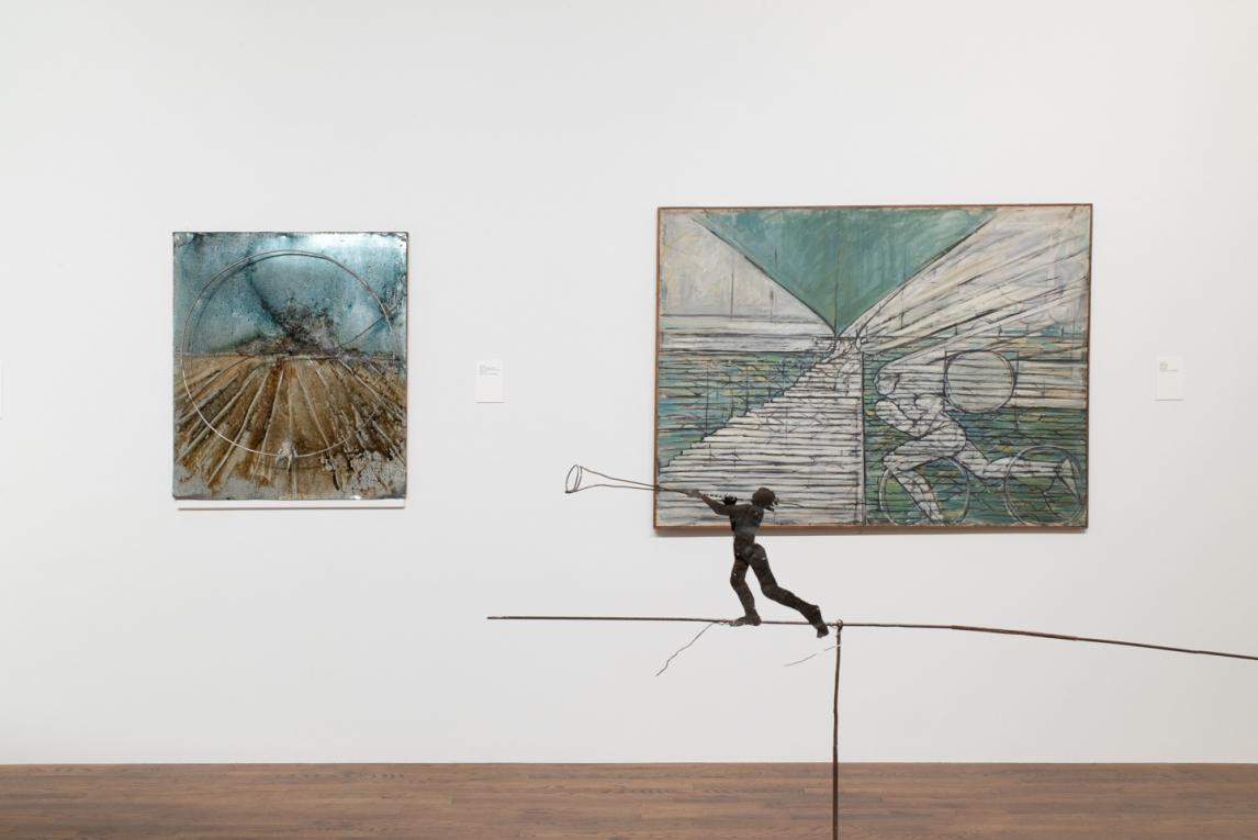 A painting and a metal work hanging next to one another on wall, with metal. sculpture in foreground