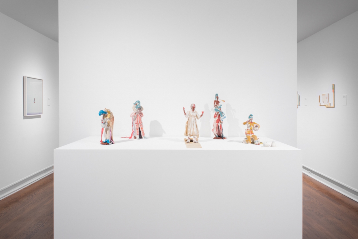 Five sculptures depicting figures, displayed on a pedestal