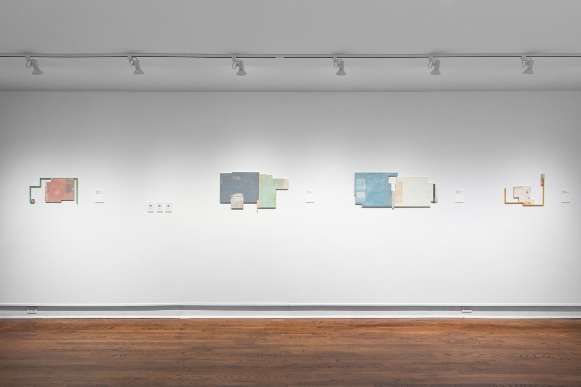 Installation view of four mixed media artworks displayed in row on wall
