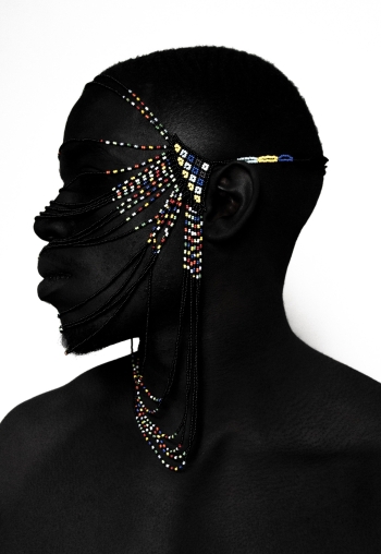 A closeup of a Black man wearing a beaded multicolored headdress over their face