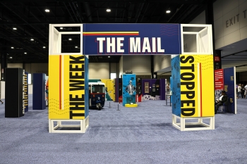 A freestanding and white exhibition gateway featuring yellow and red banners and blue and red and yellow that say The Week the Mail Stopped