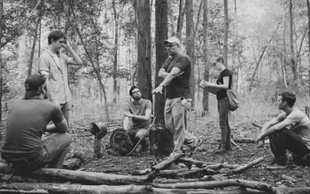 A black and white photo of David Greenberg standing in the woods and surrounded by members of his film crew