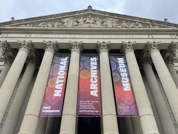 The exterior of the National Archives Museum decorated with banners in a red and yellow and purple and blue gradient with white text that displays the name of the museum 