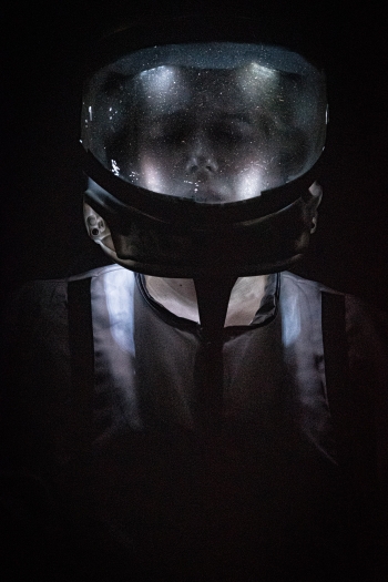 A performer in the helmet of an astronaut and only lit from within the helmet