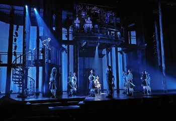 A stage set lit entirely in blue and made of stairs and beams with a cast performing on it