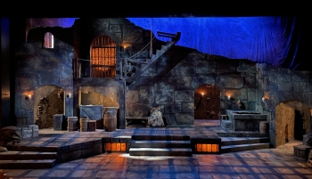 A dramatically lit stage that includes a stone medieval street scene with warm orange lights