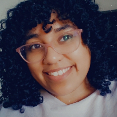 headshot of tiphany jackson. tiphany is smiling and looking towards the upper right. tiphany has thick black curly hair and is wearing pinkish horn-rimmed glasses. 