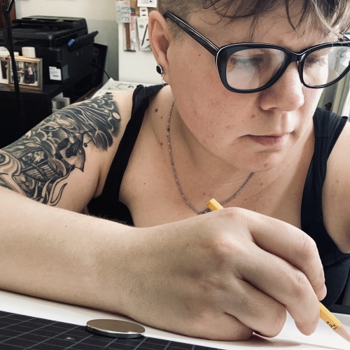 A closeup of C. Larsen drawing on paper with a pencil and wearing a black tank top