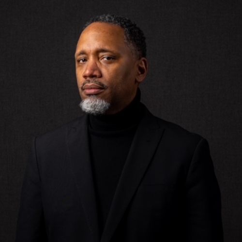 Shawn Theodore Jackson in a black turtleneck and black blazer standing in front of a black backdrop